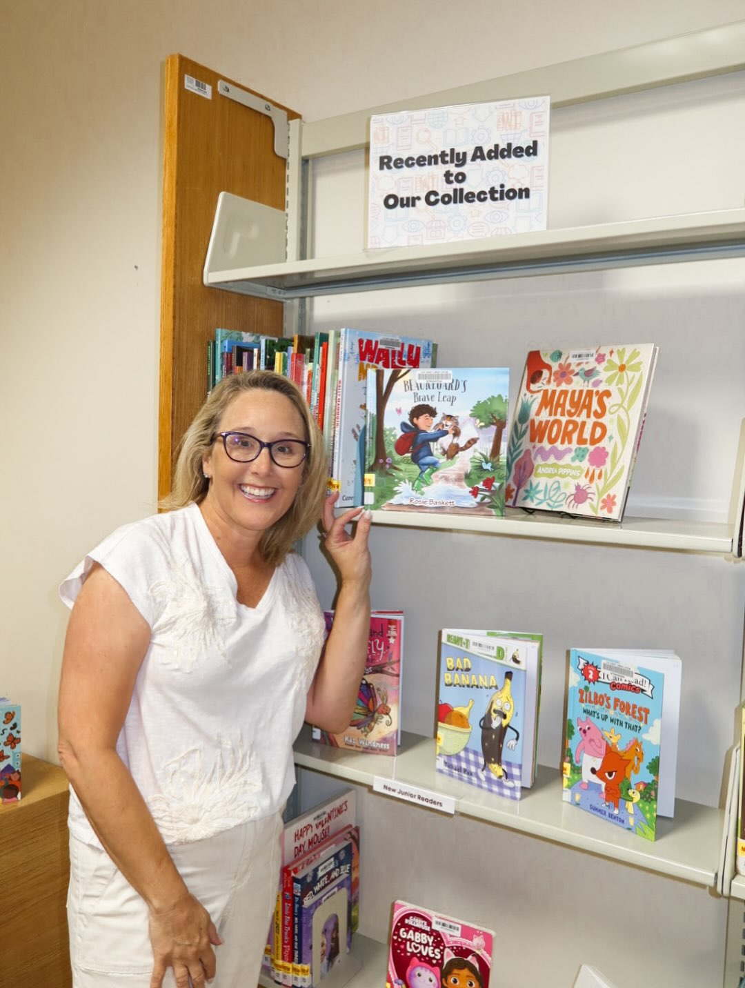Rosie Baskett beside a library shelf displaying her book among recently added titles.